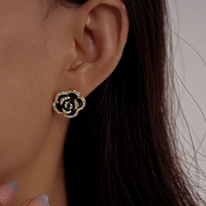 Close-up of black camellia stud earrings with gold edges and sparkling rhinestones