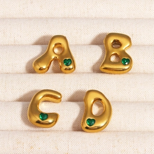 Pendentifs alphabet dorés A-D avec pierres précieuses cœur vert sur tissu beige
