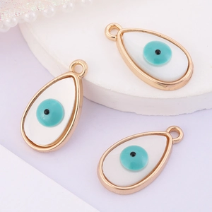 Macro shot of three teardrop-shaped white evil eye charms with golden frames for DIY jewelry