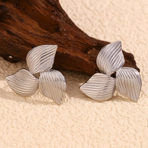 Detailed macro view of silver floral earrings with brushed metal texture on driftwood