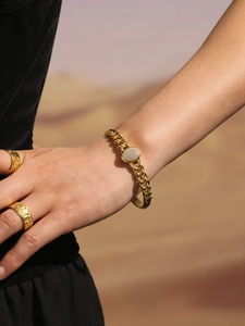 Detail of 18K gold-plated Cuban link bracelet and textured rings on model against desert backdrop