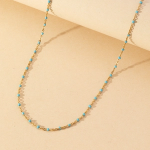 Close-up of golden necklace featuring small turquoise enamel beads on a thin chain