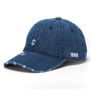 Close-up of embroidered white letter C and 1999 on distressed blue denim baseball cap