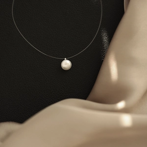 Macro detail of a single white pearl pendant on transparent fishing line necklace