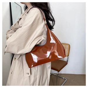 Close-up of a glossy caramel patent leather baguette bag styled with a beige trench coat