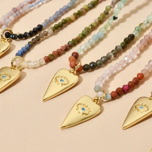 Bohemian tourmaline beaded necklace with gold evil eye pendant on beige background