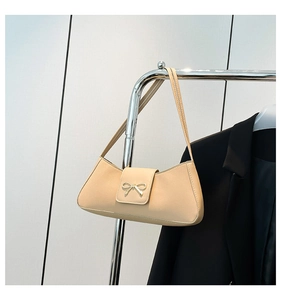 Detail of khaki baguette bag with golden bow ornament on a metal display stand