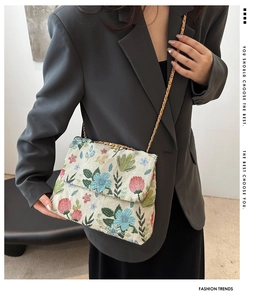Detail of floral embroidery on beige crossbody bag with gold chain strap on model