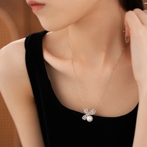 Gros plan d'un collier argenté avec pendentif nœud et perle porté sur la clavicule
