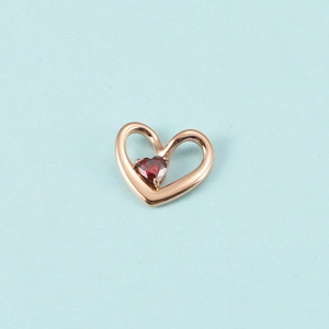 Pendentif cœur en or rose avec une petite pierre de naissance rouge sur fond bleu