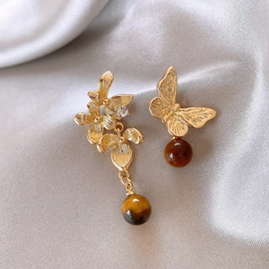 Close-up of asymmetric gold flower earrings with tiger eye beads on grey satin fabric