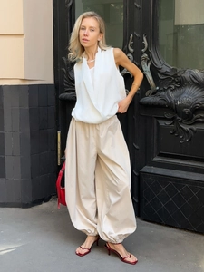 Detail of loose beige cotton harem pants with drawstring cuffs and a sleek white V-neck top