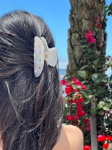Dettaglio macro di farfalle e motivi floreali su una clip per capelli bianco perla