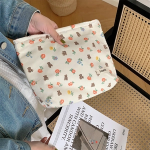 Detail showing hands holding a floral beige cotton makeup bag with cute brown bear patterns