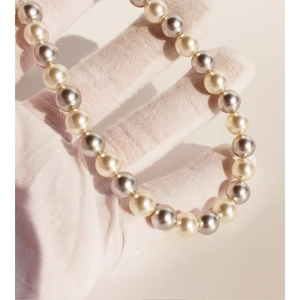 Elegant champagne and grey round pearl necklace held in white gloved hands on beige background