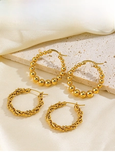 Détail de boucles d'oreilles créoles dorées perlées et torsadées sur soie et pierre beige