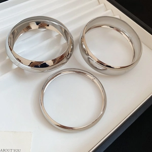 Vue macro de trois bracelets joncs minimalistes en argent poli sur un plateau blanc chic