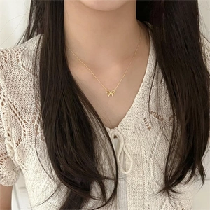 Close-up of a delicate gold bow pendant necklace worn by a model on a white lace top