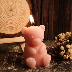 Pink sitting bear scented candle burning on rustic wood background with dried flowers