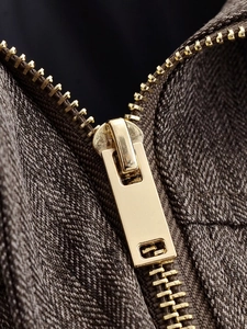 Detailed macro view of a golden metal zipper on coffee brown herringbone fabric jacket