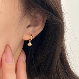 Close-up of golden teardrop earring worn on ear showing high-shine metal texture