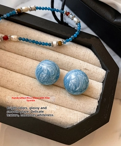 Gros plan de boucles d'oreilles boules bleues émaillées pailletées sur un plateau
