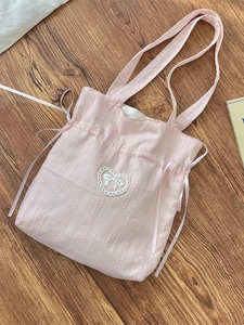 Pink drawstring canvas tote bag with ribbon bow and heart lace detail on wooden background