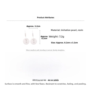 Detail view of long hook earrings featuring white resin pendants and faux pearl beads