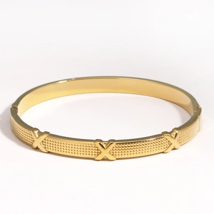 Détails d'un bracelet en acier titane doré avec symboles en X et fermeture à charnière