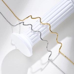 Detail of wavy gold and silver minimalist necklaces draped over a white Roman column