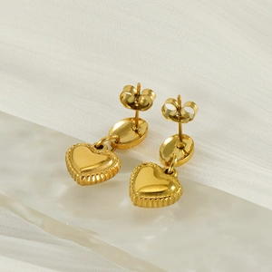 Détail de boucles d'oreilles cœur dorées avec bords à rayures verticales sur tissu blanc