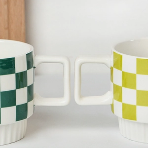 Detail of green and yellow checkered ceramic mugs with square handles and stackable bases