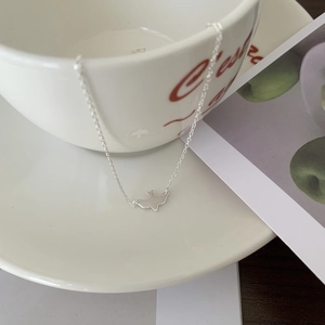 Detailed view of silver bird pendant necklace draped on a white ceramic cup