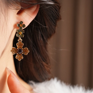 Vue rapprochée d'une boucle d'oreille croix vintage avec cristaux ambre et verts sur l'oreille