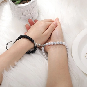 Close-up of magnetic heart charms linking tiger eye and matte bead bracelets for couples