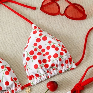 Detail of white cherry bikini top with red ties and a small golden clover charm