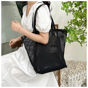 Close-up of black mesh tote bag with leather straps worn by model against a white wall