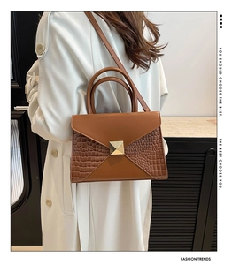 Detail of brown crocodile pattern handbag featuring a gold pyramid clasp and envelope flap