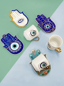 Vista dall'alto di tazzine da caffè Evil Eye e piattini Hamsa in ceramica con bordo d'oro