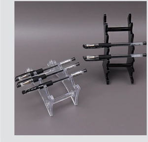 Clear and black acrylic pen display stand holding six stationery pens on grey background