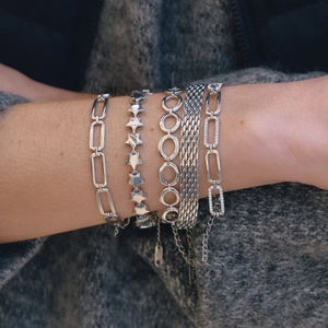 Close-up of five-piece silver bracelet set with star and paperclip chain on model wrist