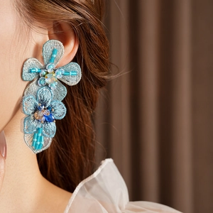 Close-up of blue embroidered flower earring with crystal beads on a female model