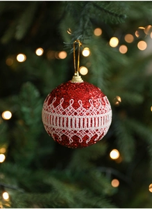 Close-up of a red glitter Christmas ball with white lace trim and gold hanging string