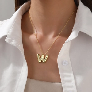 Polished 18K gold letter W pendant necklace shown on a model wearing a white shirt
