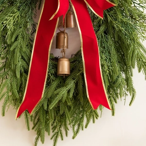 Close-up of a Christmas wreath with green pine needles, red velvet bow, and bronze bells