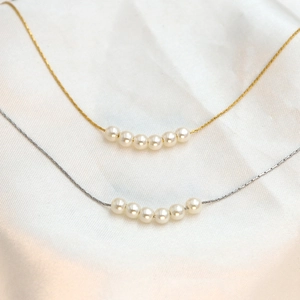 Minimalist 18k gold and silver pearl necklaces displayed on soft white silk fabric