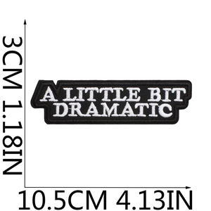 Embroidered black patch with white A Little Bit Dramatic text and size measurements