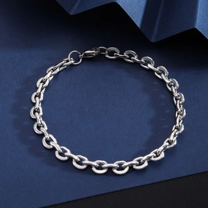Macro shot of silver stainless steel Cuban chain link bracelet on dark blue paper