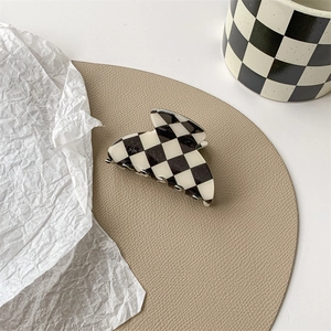 Close-up of a black and white checkerboard hair claw clip on a leather pad with aesthetic decor