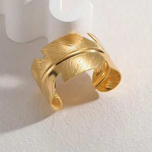 Macro detail of golden feather open bangle with brushed metal texture and polished spine